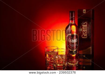 Bottle of Grant's whisky and two glasses with whisky and ices on a red background with yellow ligthing. Copy space.