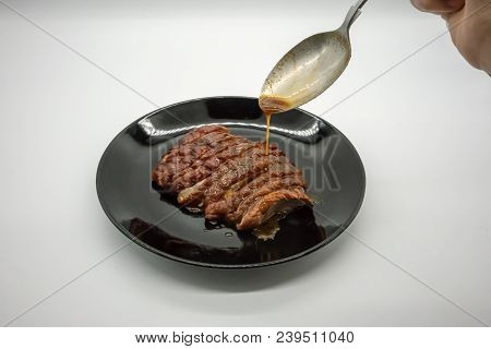 Woman Hand Holding Silver Spoon Adding Sauce On Top Of Roasted Duck On Black Ceramic Dish Isolated O