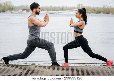 Well-built And Gorgeous People Are Posing At The Adge Of The River On The Bridge. They Are Squating 