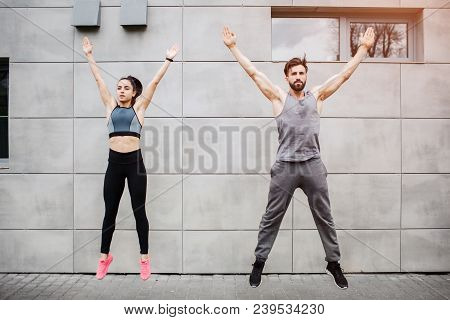Handsome Man And Beautiful Girl Is Jumping Near Cocnrete Wall. They Are Keeping Their Hands Over The