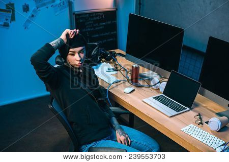 Young Female Hacker At In Front Of Desk Taking Off Mask