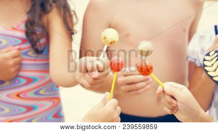 Cute Brother And Sisters Enjoying Their Lollipops Outside At The Beach.