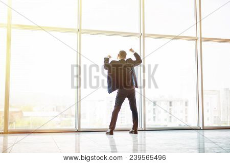 Excited Middle Age Businessman With Victory Reised Hands Up In Front Of Panoramic Window On Sunset