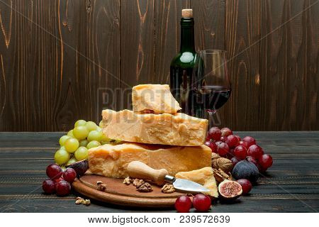 Pieces Of Parmesan Or Parmigiano Hard Cheese, Grapes And Wine On Wooden Cutting Board