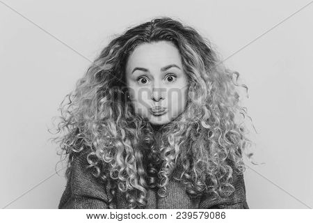 Fuuny Blonde Female With Curly Hair, Blows Cheeks And Stares At Camera, Reacts Actively On Unexpecte