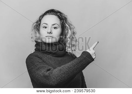 Check This Out. Serious Blonde Young Woman With Curly Blonde Hair Dressed In Bright Blue Sweater, In