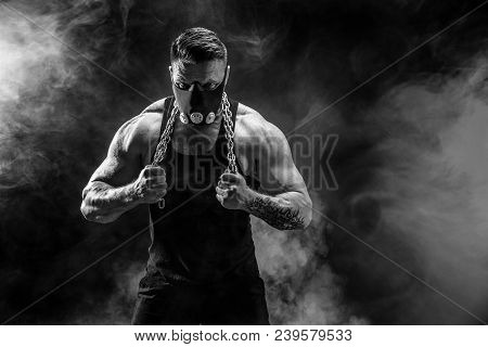 Portrait Of Muscular Sportsman In Training Mask Hold Metal Chain.black Background With Smoke