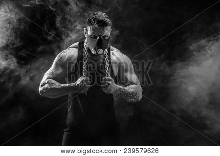 Portrait Of Muscular Sportsman In Training Mask Hold Metal Chain.black Background With Smoke