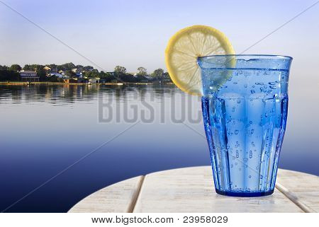 Um vidro azul com água com gás e limão em um Deck de madeira com vista para o mar calmo de um Tropica