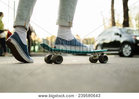 Side View Of The Young Hepcat In Blue Jeans And Canvas Skate Shoes Crossing The Road With Blue Plast