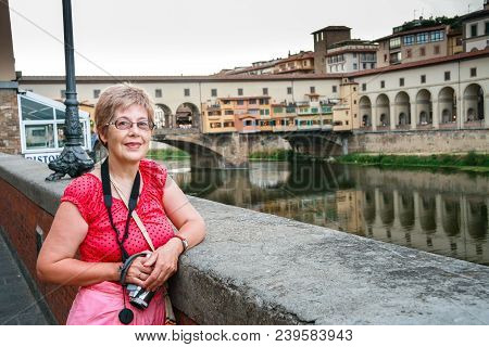 Mature Tourist Woman Travelling In Italy With Video Camera On Her Neck Stays Against Ponte Vecchio B
