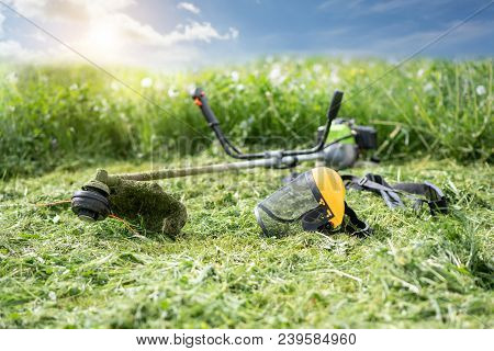 String Trimmer And Protective Face Mask On Mown Grass, Growing Grass And The Blue Sky On The Backgro