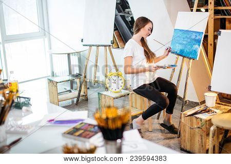 Classes In Art Studio. Pretty Young Student Girl With Long Dark Hair, Dressed Casually, Painting