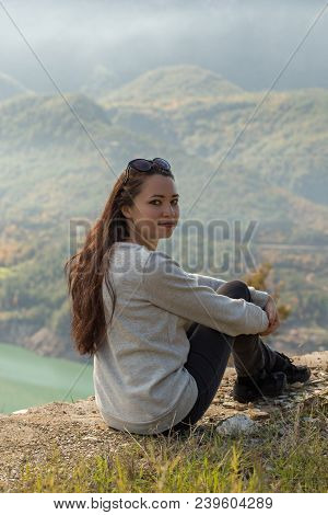 Solo Female Traveller Sitting At The Roof Of Stone Building Against The Picturesque Mountain View