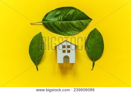 Miniature Toy Model House With Green Leaves On Yellow Colourful Trendy Backgdrop. Eco Village, Abstr