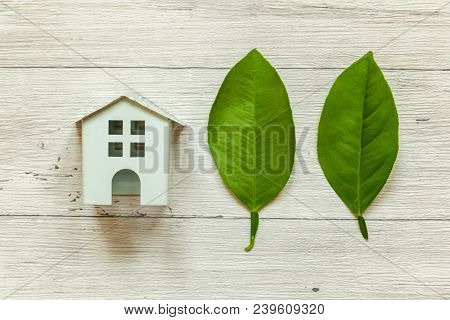 Miniature White Toy Model House With Green Leaves On Wooden Backgdrop. Eco Village, Abstract Environ