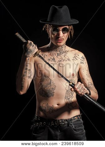 Man With Naked Tattooed Torso In Hat Holding Sword Katana In Hands On Black Background. Defense, Hon