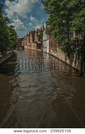 Wooded Gardens And Brick Buildings On The Canal Edge In A Sunny Day At Bruges. With Many Canals And 