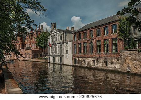 Wooded Gardens And Brick Buildings On The Canal Edge In A Sunny Day At Bruges. With Many Canals And 