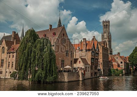 Boats And Leafy Tree With Brick Buildings On The Canal Edge In A Sunny Day At Bruges. With Many Cana
