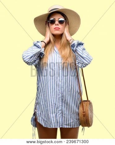 Young woman wearing sunglasses and summer hat covering ears ignoring annoying loud noise, plugs ears to avoid hearing sound. Noisy music is a problem.