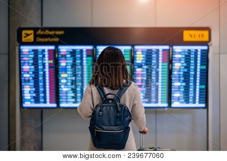 Young Woman Traveler With Backpack And Luggage Looking At Boarding Time At Departure Board At Termin