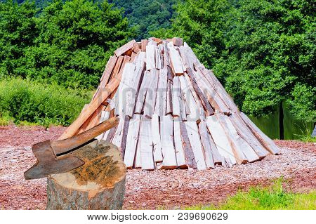 Conical Stacked Logs, Firewood Storage For The Winter. In The Foreground A Hack Wood With Ax.