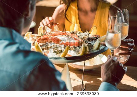 Close-up of fresh oysters and crabs served on ice with lemon at the table of a romantic couple in love, celebrating with champagne at a trendy restaurant