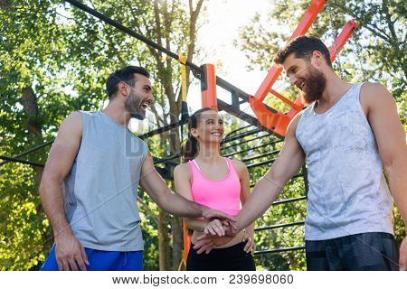 Low-angle view of three cheerful young friends putting hands together as a gesture of determination and motivation for starting street workout together in summer