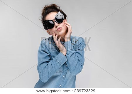 Young Girl In Black Cat Glasses On A Gray Background. Portrait Of A Young Beautiful Girl. Charming G