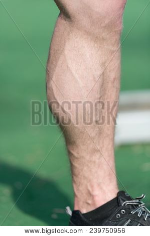 Muscular Leg With Vein At Stadium Or Arena On Sunny Outdoor. Foot In Black Sport Fashion Shoe On Gre