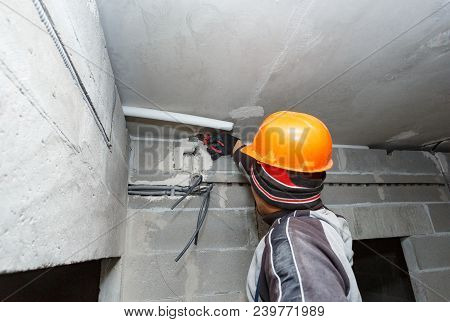 The Worker In The Helmet Is Laying Electrical Wiring During The Roughing Phase.