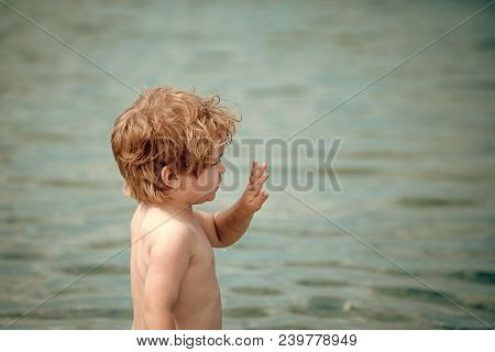 Cute Child Waving Hand, At Seashore. Boy With Serious Face Stand Near Sea Water. Farewell And Partin