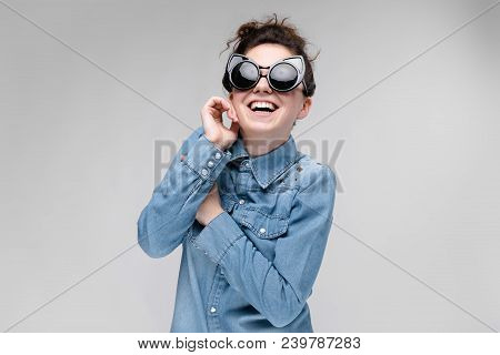Young Girl In Black Cat Glasses On A Gray Background. Portrait Of A Young Beautiful Girl. Charming G