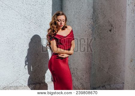 Beautiful Young Woman In A Long Red Evening Gown With A Train Standing Next To The Old Wall