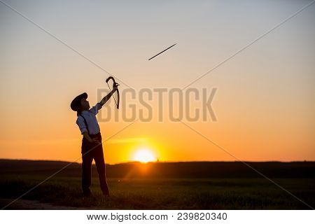 Silhouette Of Child Playing With Bow And Arrows, Archery Shoots A Bow At The Target.