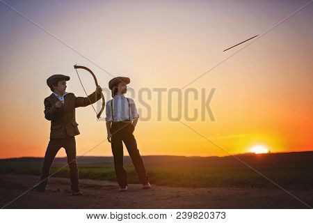 Silhouette Of Child Playing With Bow And Arrows, Archery Shoots A Bow At The Target.