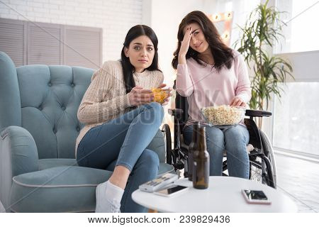 Too Scary. Startled Sister And Disabled Woman Regarding Movie And Consuming Popcorn With Cheeps