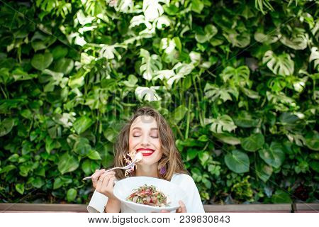 Young And Beautiful Woman Enjoying Heathy Salad Sitting At The Vegetarian Restaurant With Living Wal