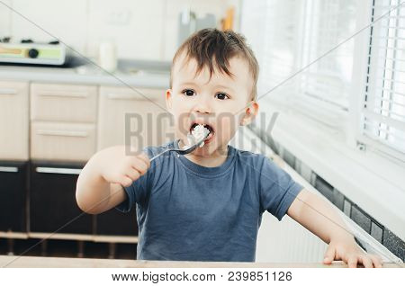 The Little Boy In The Kitchen Eagerly Eating Rice With A Spoon Independently