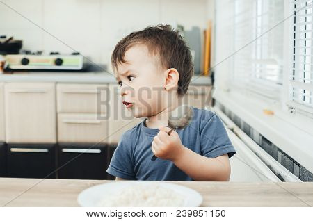 The Little Boy In The Kitchen Eagerly Eating Rice With A Spoon Independently