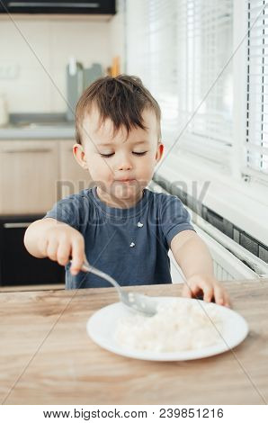 The Little Boy In The Kitchen Eagerly Eating Rice With A Spoon Independently