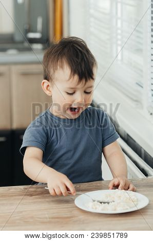 The Little Boy In The Kitchen Eagerly Eating Rice With A Spoon Independently