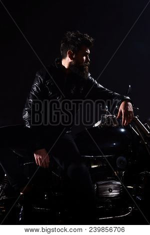 Man With Beard, Biker In Leather Jacket Lean On Motor Bike In Darkness, Black Background. Brutality 