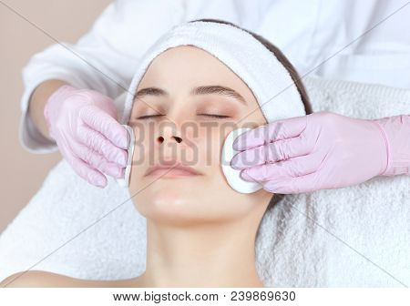 The Doctor Cosmetologist Cleanses With A Tonic The Face Skin Of A Beautiful, Young Woman In A Beauty