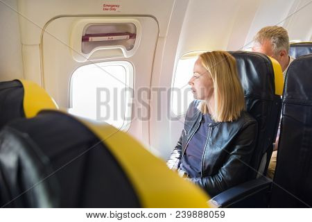 Woman Looking Through The Window On Airplane During Flight. Female Traveler Seated In Passanger Cabi