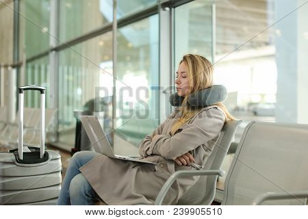 Pretty Woman Sitting In Waiting Room With Laptop And Using Social Networks Near Valise, Using Neck P