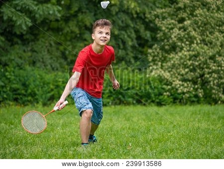 Young Teen Boy Playing Badminton In Meadow With Forest In Background. Child With Badminton Rackets I
