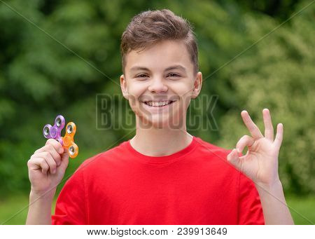 Young Teen Boy Holding Popular Fidget Spinner Toy - Outdoors Portrait. Happy Smiling Child Making Ok
