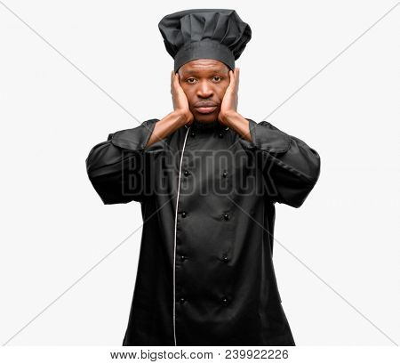 Young black cook wearing chef hat covering ears ignoring annoying loud noise, plugs ears to avoid hearing sound. Noisy music is a problem.